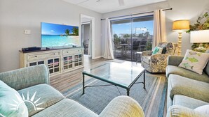 A living room with a television, a ceiling fan, a glass table, and a view of the ocean through a sliding door. - Island South 27- Updated, Spacious 2 bedroom condo with ocean view, pool and (St. Augustine)