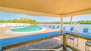 Un área de piscina con un jacuzzi, sillas de descanso y una terraza techada.