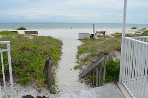 Stroll along the beach entrance pathway, lined with benches and bordered by fences, leading to a serene sandy beach.