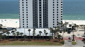 A high-rise hotel with multiple floors, a beach view, and a parking area with palm trees. - Upgrades Galore! STUNNING Views, Steps to the Sand & Short Walk to FLORA-BAMA!! (Orange Beach)