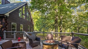 A wooden cabin with a deck featuring wicker furniture and a central fire pit.