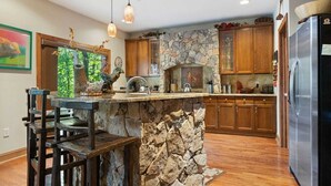 A kitchen with a stone island, wooden cabinets, and a stainless steel refrigerator.