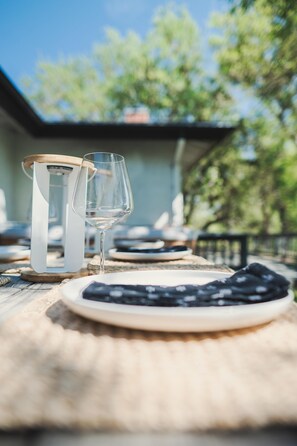 A dining table with a wine glass and a bottle opener, set outdoors with a view of trees and a building in the background. - Ranch House Estate - Hilltop ranch house — pool, tennis, vineyard views, 4 bed / 2.5 bath (Paso Robles)