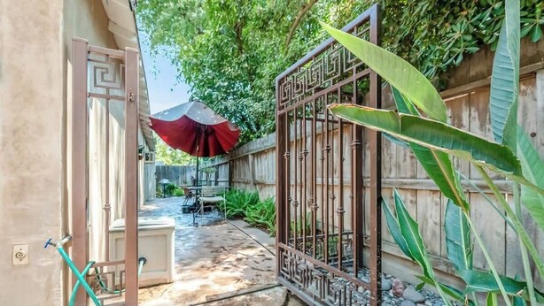 A gated backyard with a concrete patio, a red umbrella, and a metal gate.