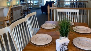 Een eetgedeelte met een houten tafel voor vier personen, omringd door witte stoelen.