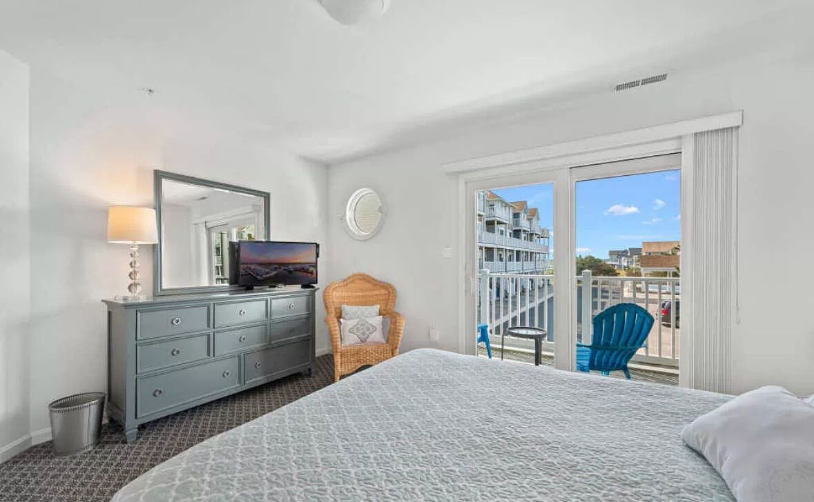 A hotel room with a bed, dresser, mirror, and a balcony with a view of buildings.