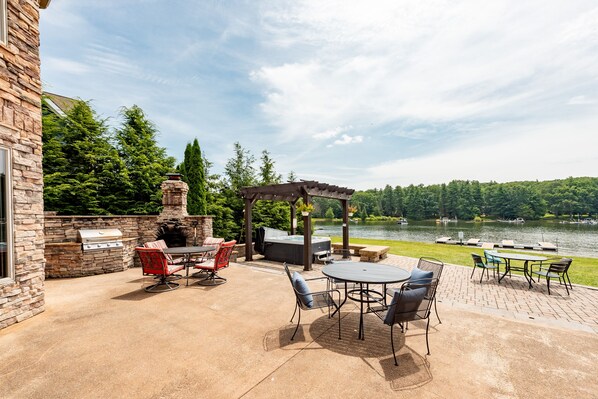 An outdoor patio with a grill, seating, and a view of a lake.