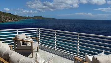 A deck with outdoor furniture, a railing, and a view of the ocean and distant land.