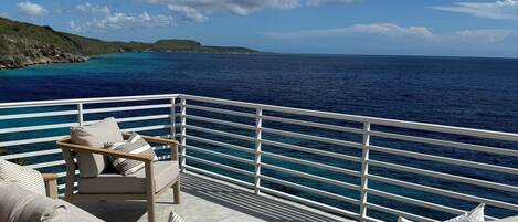 Una terraza con mobiliario exterior, barandilla y vista al océano y la costa lejana.