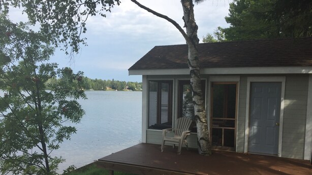 Una cabaña junto al lago con un balcón, una silla y una puerta que da al interior.