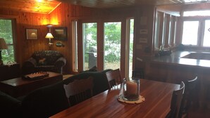 Interior de una cabaña de madera con una mesa de comedor, sillas, un sofá y una zona de cocina.