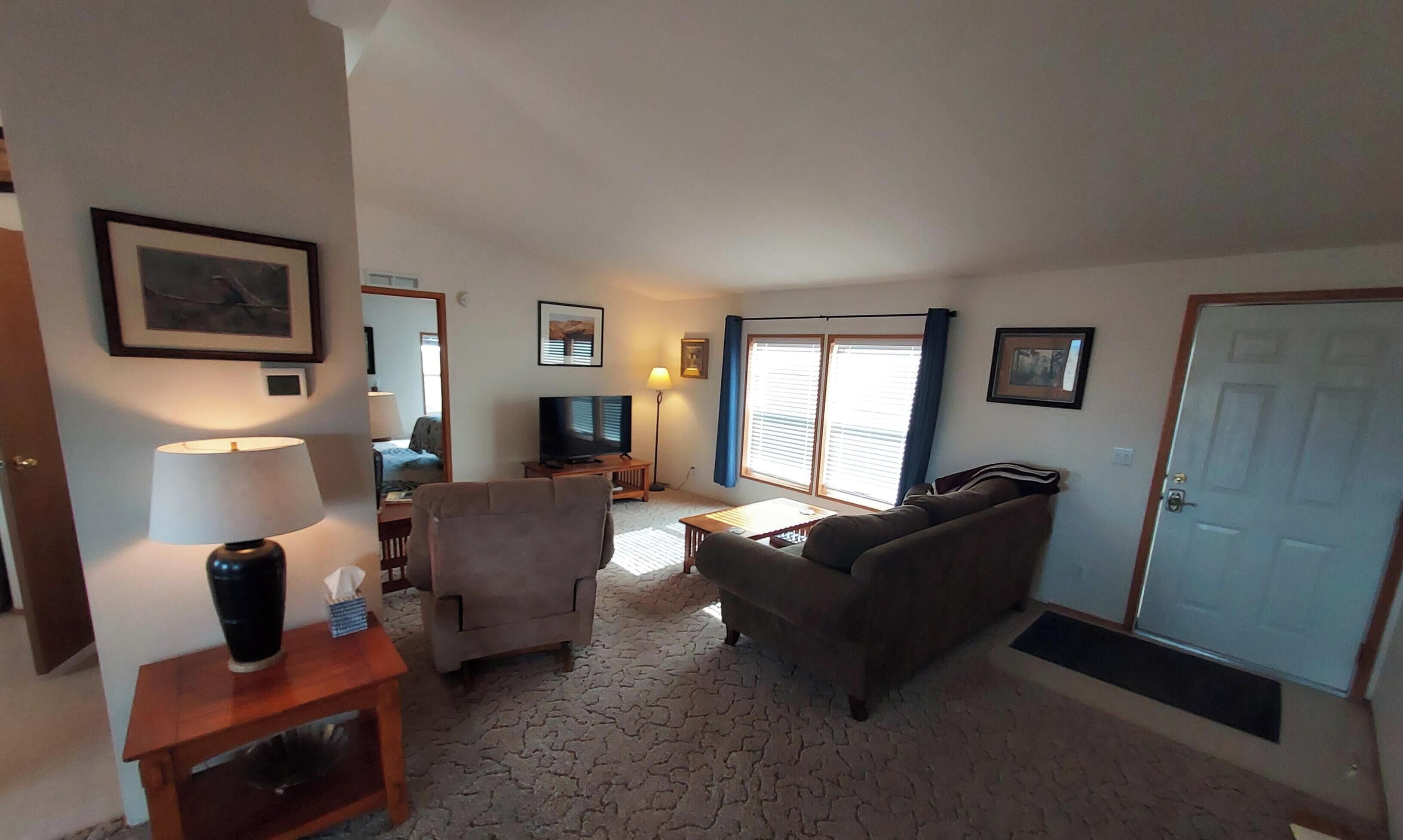 Una sala de estar con sofá, sillón, televisor y una puerta.