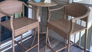 A porch with wicker furniture, a small table, and two signs reading "HOME IS WHERE YOU PARK YOUR FLIP FLOPS" and "BEACH HOUSE". - 2 story condo w/ Stunning Views and Many Amenities (Ocean View)