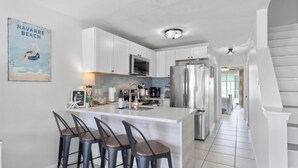 Une cuisine moderne avec des meubles blancs, un réfrigérateur en acier inoxydable et un coin bar équipé de tabourets.