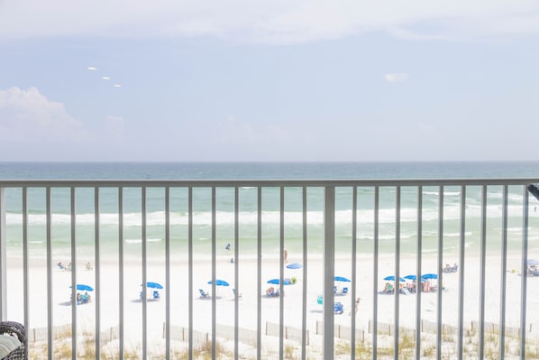 Uitzicht op een strand vanaf een balkon met een hekwerk, zandstrand en oceaan.