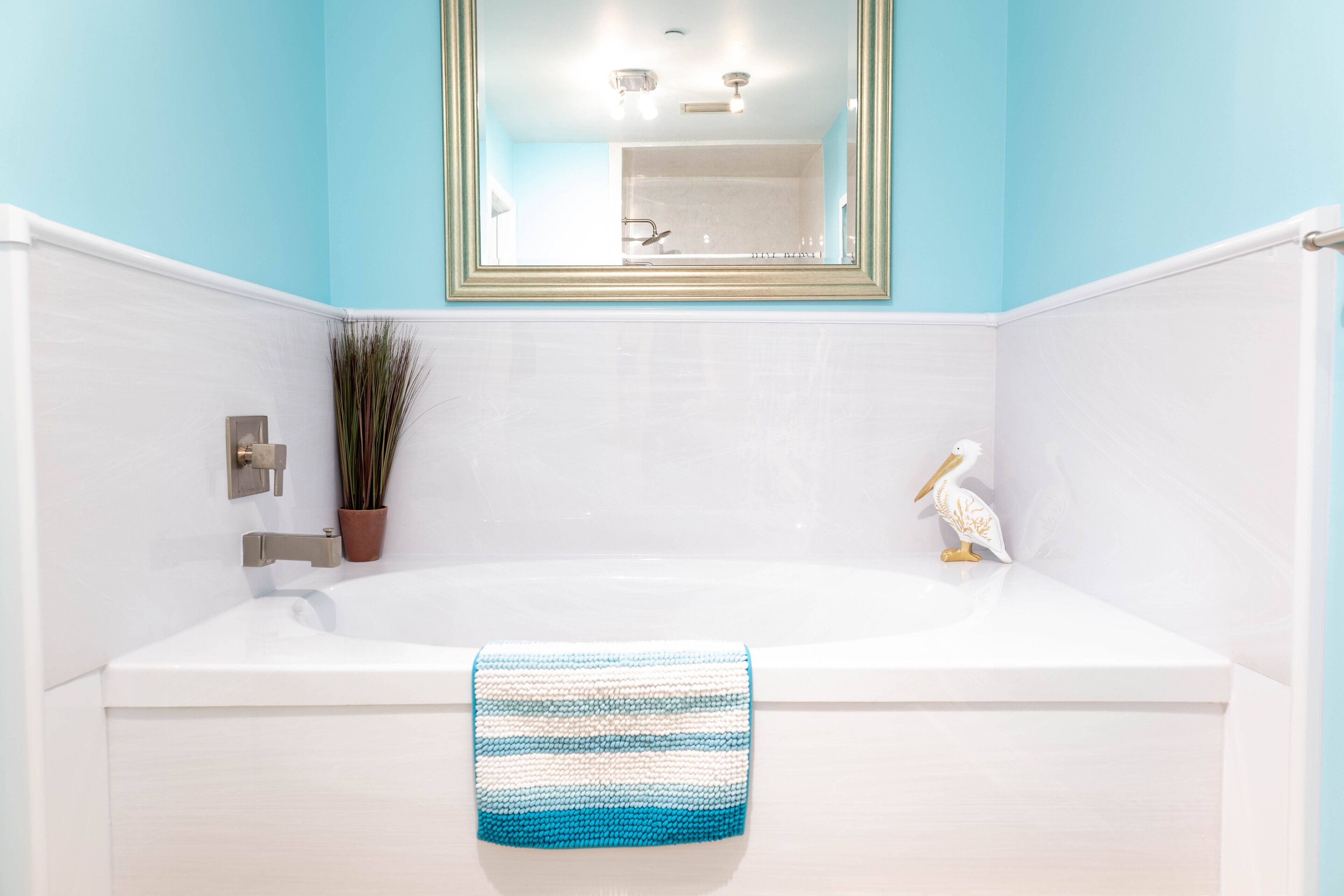 Een badkamer met een witte badkuip, een blauw-witte handdoek, een kamerplant en een decoratief vogelbeeldje.