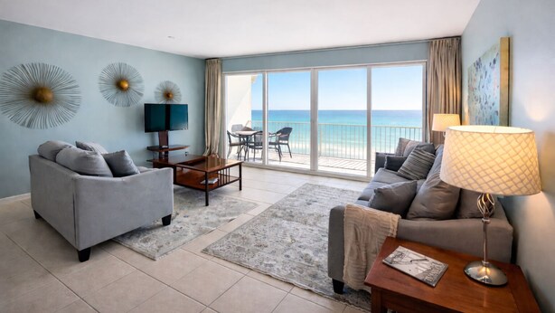 A spacious living room with a large sliding glass door leading to a balcony with a view of the ocean. There are two sofas, a coffee table, and a TV. - Wow!!!  Updated Beach front 4th top flr condo RIGHT on the beach (Destin)