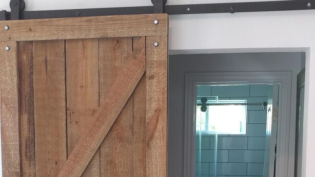 A wooden barn-style door with a metal handle, leading to a room with a tiled floor and a door with a handle. - Texas Loft is an upstairs studio efficiency apartment (McKinney)