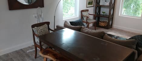 A dining area with a wooden table and benches, a sofa with patterned cushions, and a large mirror on the wall.