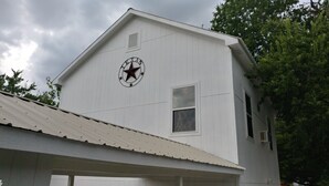 A white building with a star emblem on the side, a small window, and a metal roof. - Texas Loft is an upstairs studio efficiency apartment (McKinney)