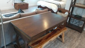 A cozy living area with a wooden coffee table, a sofa, and a bench. A bed with a white comforter is in the background. - Texas Loft is an upstairs studio efficiency apartment (McKinney)