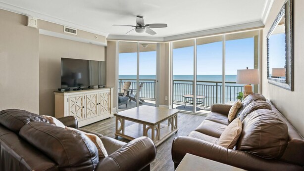 A spacious living room with a large TV, leather sofas, a coffee table, and a balcony with a view of the ocean. - Luxury Oceanfront Condo, Jacuzzi Tub, Lazy River | Mar Vista Grande - 1110 (North Myrtle Beach)