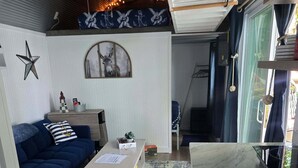 Un salon avec un canapé bleu, une petite table, un tapis et une vue sur l’extérieur par une fenêtre.
