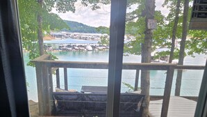 Une vue depuis une fenêtre donnant sur une terrasse en bois avec un banc, une table et un panneau indiquant : « Bienvenue à Lake House. »