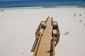 A wooden boardwalk leading to beach chairs and tables on a sandy beach with the ocean in the background. - Luxury Beachfront Home, with Ramp; Sleeps up to 18! (Gulf Shores)