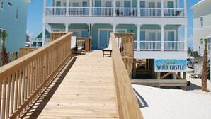A beachfront hotel with a wooden boardwalk leading to a two-story building with balconies. - Luxury Beachfront Home, with Ramp; Sleeps up to 18! (Gulf Shores)