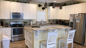 A modern kitchen with white cabinets, stainless steel appliances, and a marble island. - Luxury Beachfront Home, with Ramp; Sleeps up to 18! (Gulf Shores)