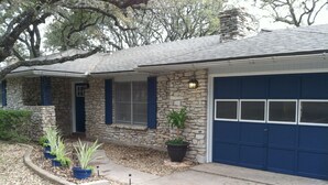 Une maison en pierre avec une porte de garage bleue, une cheminée en pierre et un pot de fleurs dans le jardin.