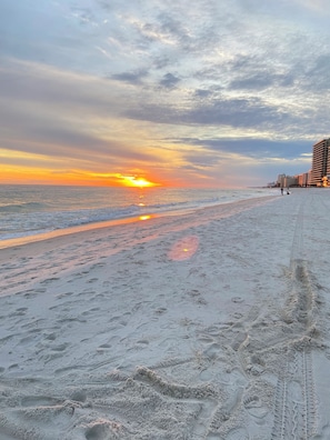 A beach with footprints, a sunset, and buildings in the background.