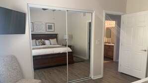 Un dormitorio con cama, una silla, un armario y un baño visible a través de una puerta abierta.