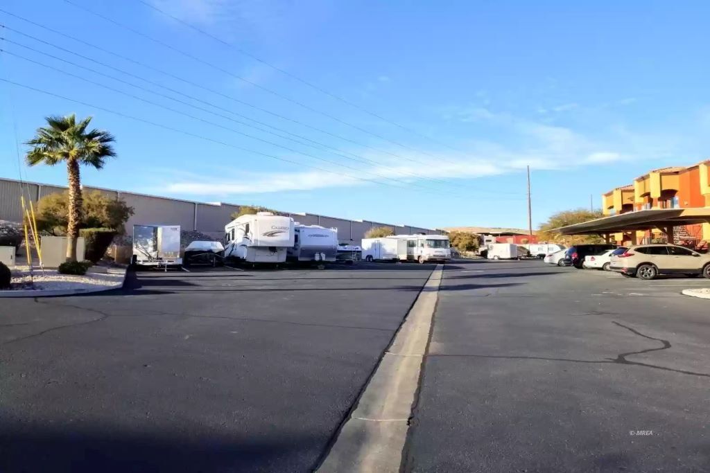 A parking lot with RVs and cars, a palm tree, and a building with a flat roof.