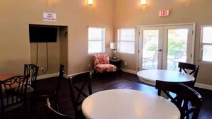 Un área de comedor con mesas y sillas, un cartel que indica vigilancia y una señal de salida.