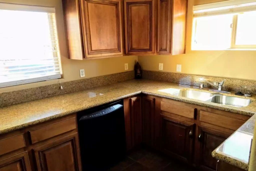 A kitchen with granite countertops, wooden cabinets, a dishwasher, and a double sink.