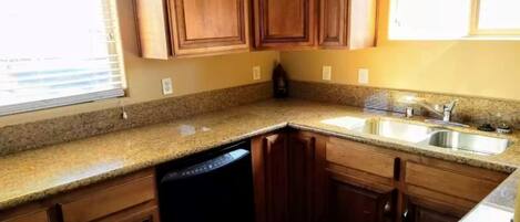 A kitchen with granite countertops, wooden cabinets, a dishwasher, and a double sink.