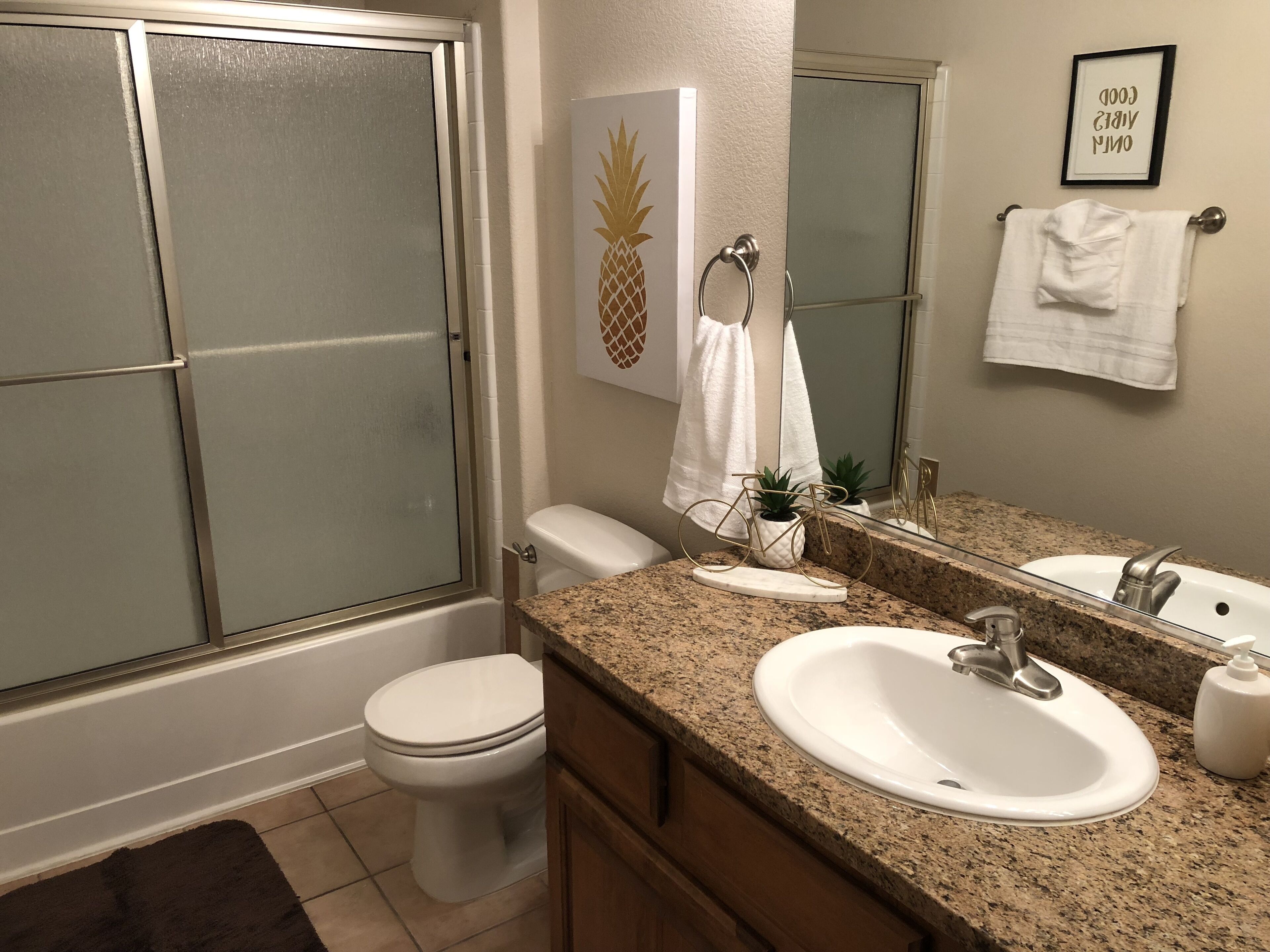 A bathroom with a toilet, sink, and shower. There is a towel rack with a towel and a framed picture on the wall.
