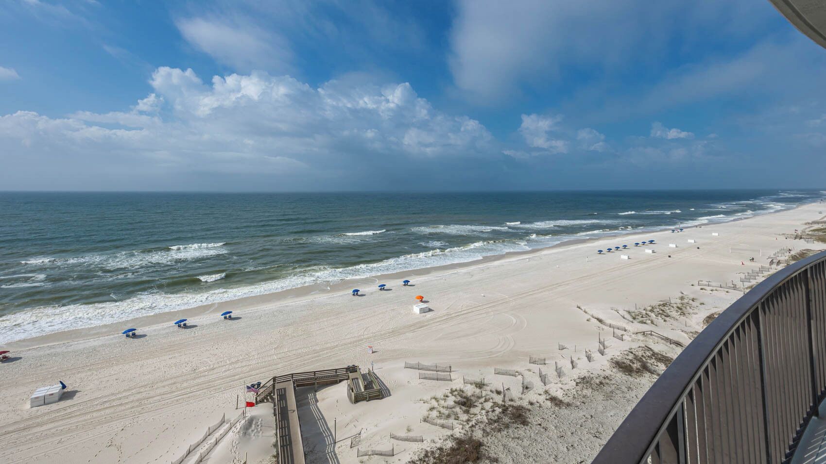 A beach with umbrellas and beach chairs, a wooden boardwalk, and a view of the ocean.
