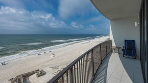 A balcony with a view of a beach, a chair, and a small table. - Phoenix IX 905 - Beautiful 3BR Gulf Front Unit (Orange Beach)