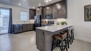 A modern kitchen with a central island, dark cabinetry, and pendant lighting. - The Lofts #7 | Townhome Pool Resort | Poolside (Saint George)