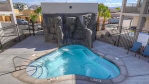 A swimming pool with a rocky waterfall feature, surrounded by a metal fence and lounge chairs. - The Lofts #7 | Townhome Pool Resort | Poolside (Saint George)