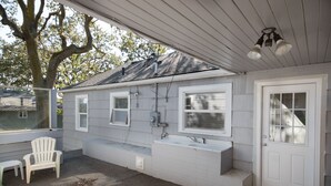 A covered outdoor area with a white door, a bench, and a small sink. - Cute, Cozy & Comfortable Cottage Conveniently Located In The Heart Of Town.  (Oak Harbor)
