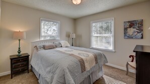 A bedroom with a bed, two windows with blinds, a nightstand with a lamp, a chair, and a painting on the wall. - Cute, Cozy & Comfortable Cottage Conveniently Located In The Heart Of Town.  (Oak Harbor)