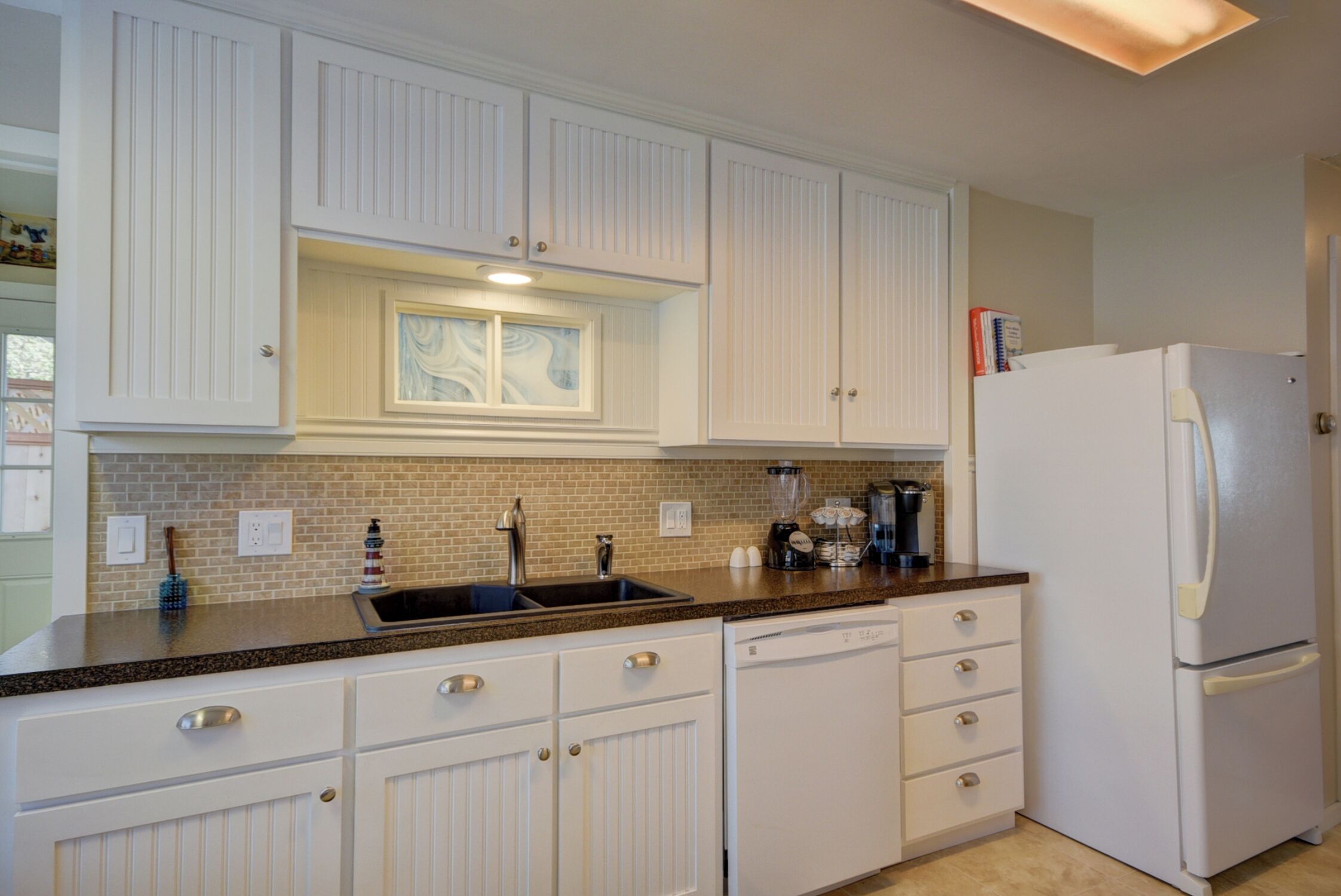 A kitchen with white cabinetry, a granite countertop, a built-in sink, and a white refrigerator.