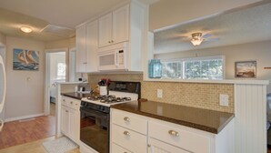 A kitchen with white cabinets, a gas stove, a microwave, and a window with blinds. - Cute, Cozy & Comfortable Cottage Conveniently Located In The Heart Of Town.  (Oak Harbor)