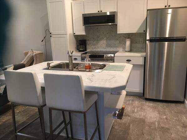 A compact kitchen with white cabinetry, a stainless steel refrigerator, a microwave, and a coffee maker. - August dates available /screen porch & fire pit /close to Downtown /Pets ok (Highlands)