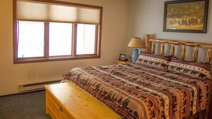 A bedroom with a large window, a bed with patterned bedding, a wooden headboard, a nightstand with a lamp, and a framed picture on the wall. - 2 Bedroom 2 bath end unit pet friendly condo in the  (mammoth lakes)