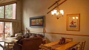 A cozy living room with a sofa, a wooden dining table, and a chandelier. There is a framed picture on the wall and a poster. - 2 Bedroom 2 bath end unit pet friendly condo in the  (mammoth lakes)